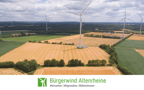 Luftaufnahme eines Feldes mit Windrädern im Hintergrund und einem Logo von Bürgerwind Altenreine am unteren Bildrand.