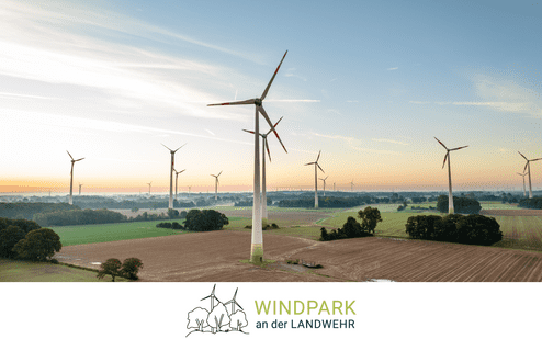 Luftaufnahme eines Windparks mit mehreren Windturbinen in einer ländlichen Landschaft bei Sonnenaufgang.