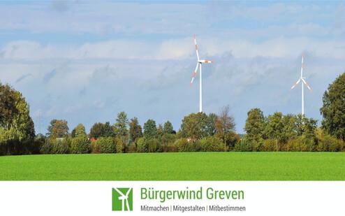 Zwei Windkraftanlagen stehen in einer grünen Landschaft unter einem blauen Himmel mit wenigen Wolken.