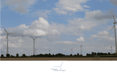 Windkraftanlagen stehen vor einem bewölkten Himmel, umgeben von landwirtschaftlichen Flächen und Bäumen.