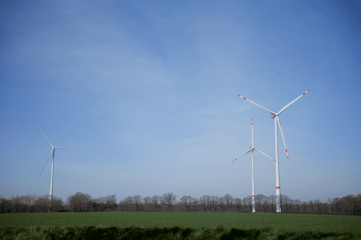 Drei Windkraftanlagen stehen auf einem grünen Feld unter einem blauen Himmel mit wenigen Wolken.