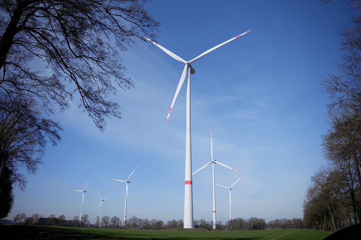 Windkraftanlagen auf einem Feld unter blauem Himmel, umgeben von Bäumen und Wiesen.
